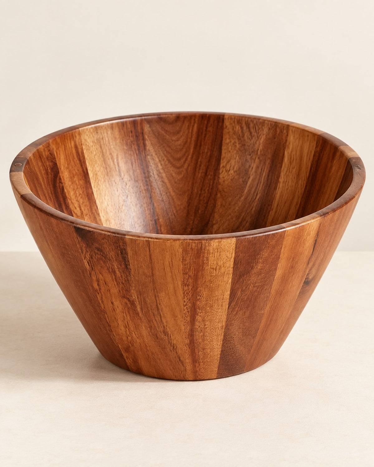 Empty acacia wood salad bowl on a warm off-white surface.