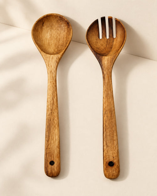 Acacia salad spoon and fork side by side on a warm off-white surface.