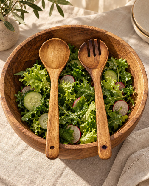 Acacia salad servers resting in a wooden salad bowl with green salad. Bowl and food not included.