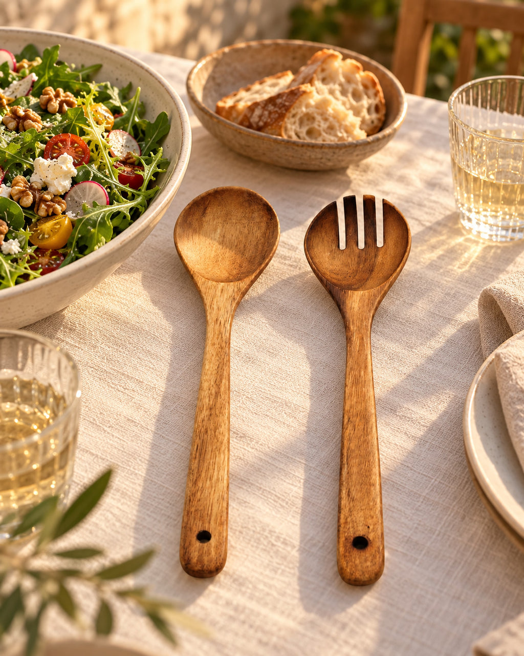 Acacia salad servers beside a salad bowl on an outdoor dinner table at golden hour.