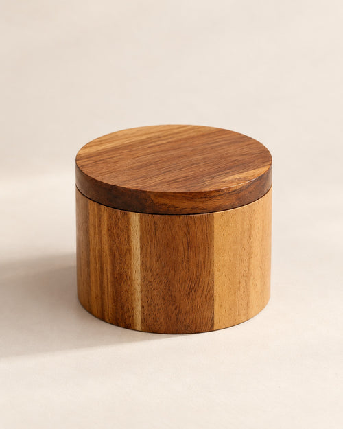 Closed round acacia salt cellar on a warm off-white surface.
