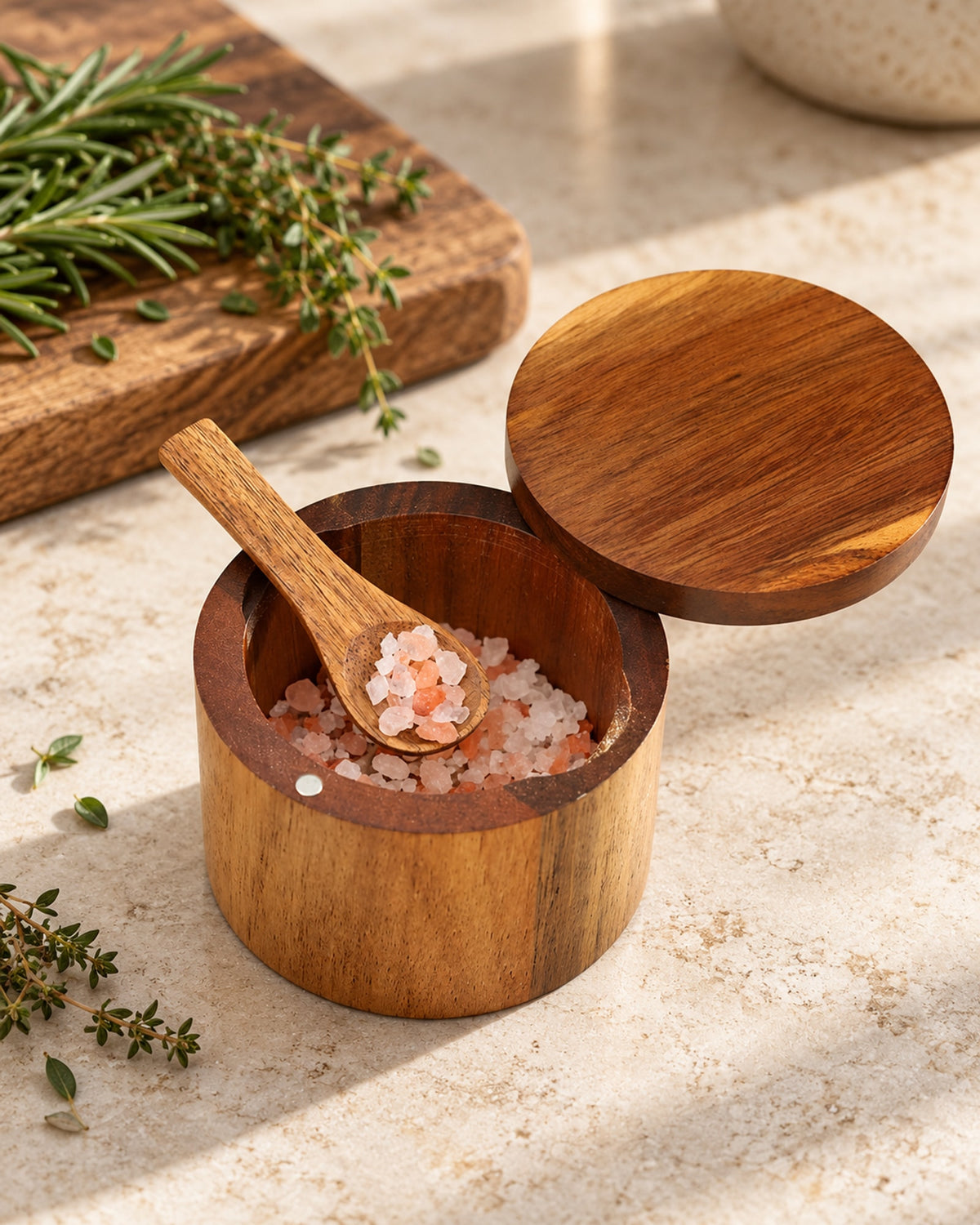 Open acacia salt cellar with flaky salt and a wooden spoon on a stone worktop. Salt not included.