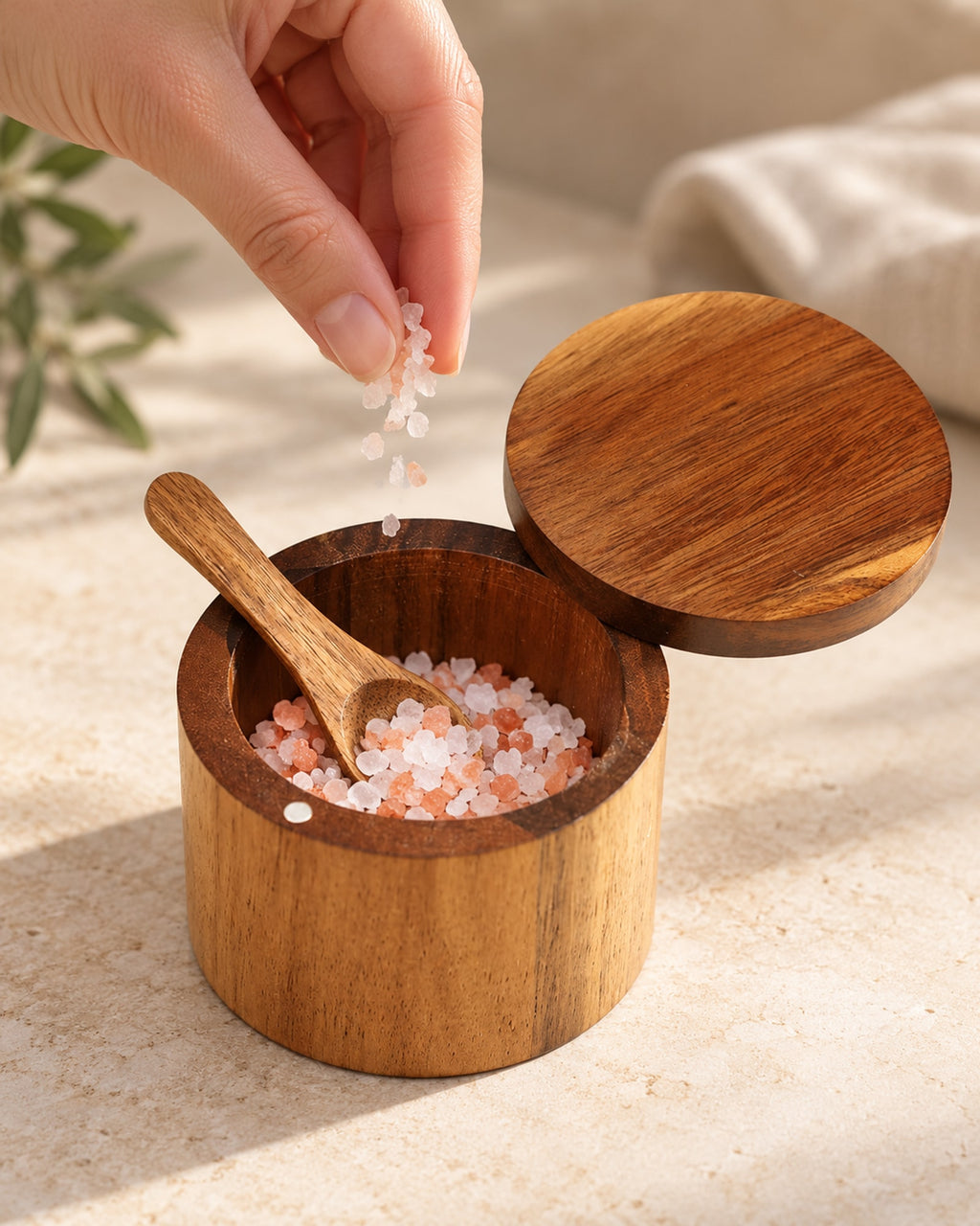 Fingers taking a pinch of salt from the acacia salt cellar.