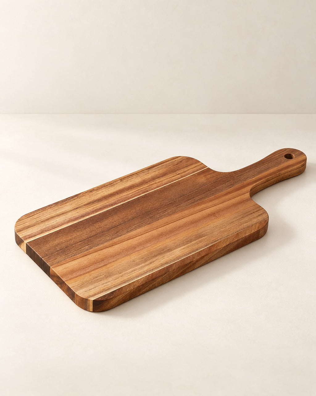 Acacia wood serving board with a handle on a warm off-white surface.