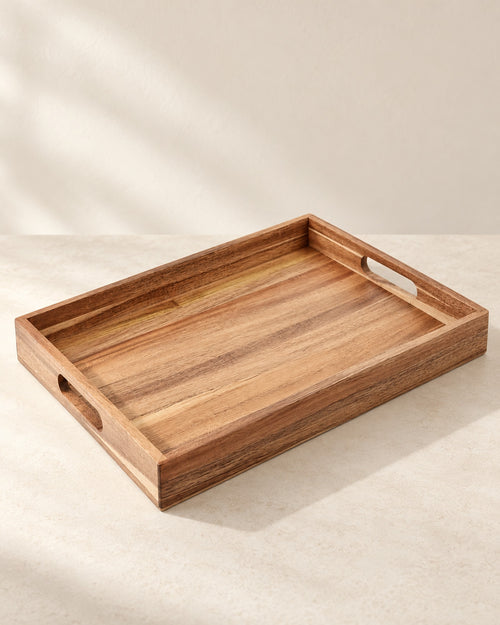 Empty acacia serving tray with cut-out handles on a warm off-white surface.