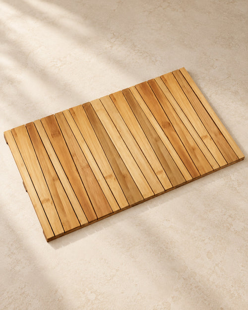 Slatted bamboo bath mat on a warm off-white floor.