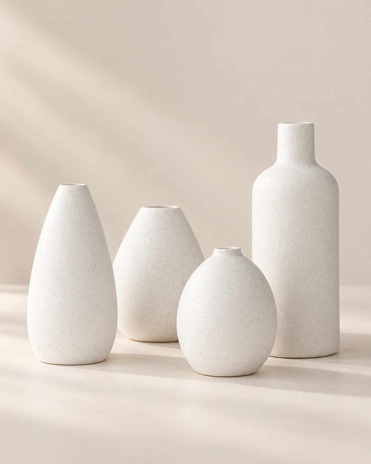 Four matte white ceramic bud vases grouped on a warm off-white surface.
