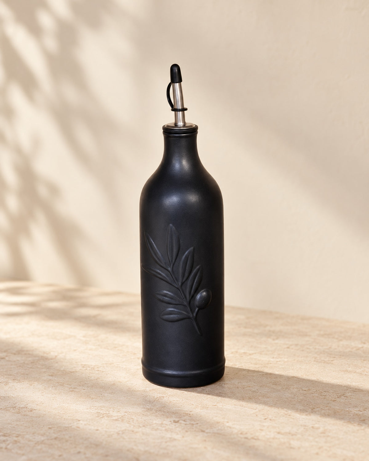 Matte black ceramic olive oil bottle on a warm off-white surface.