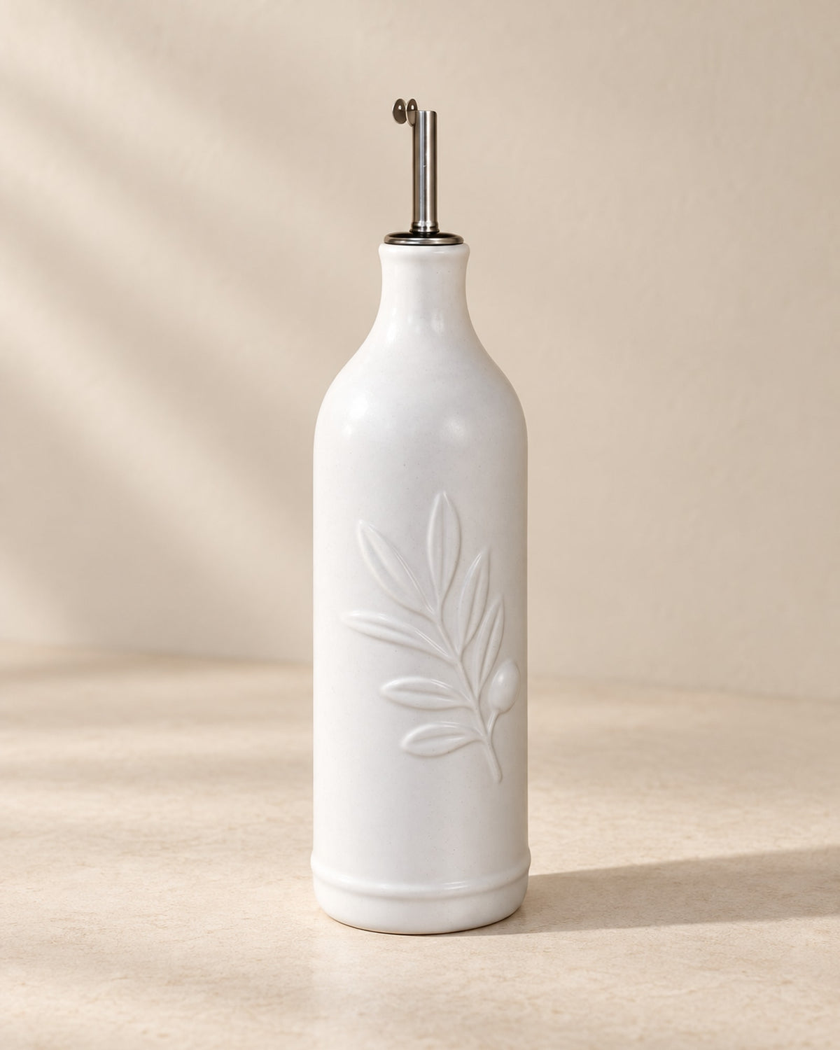 Matte white ceramic olive oil bottle on a warm off-white surface.