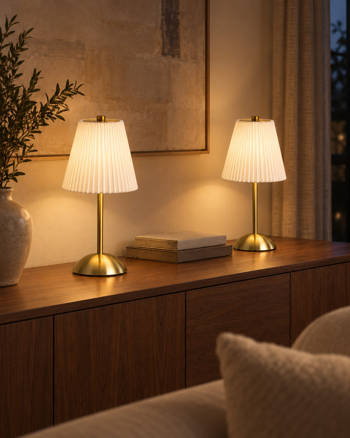 Two pleated table lamps glowing on a sideboard at night.