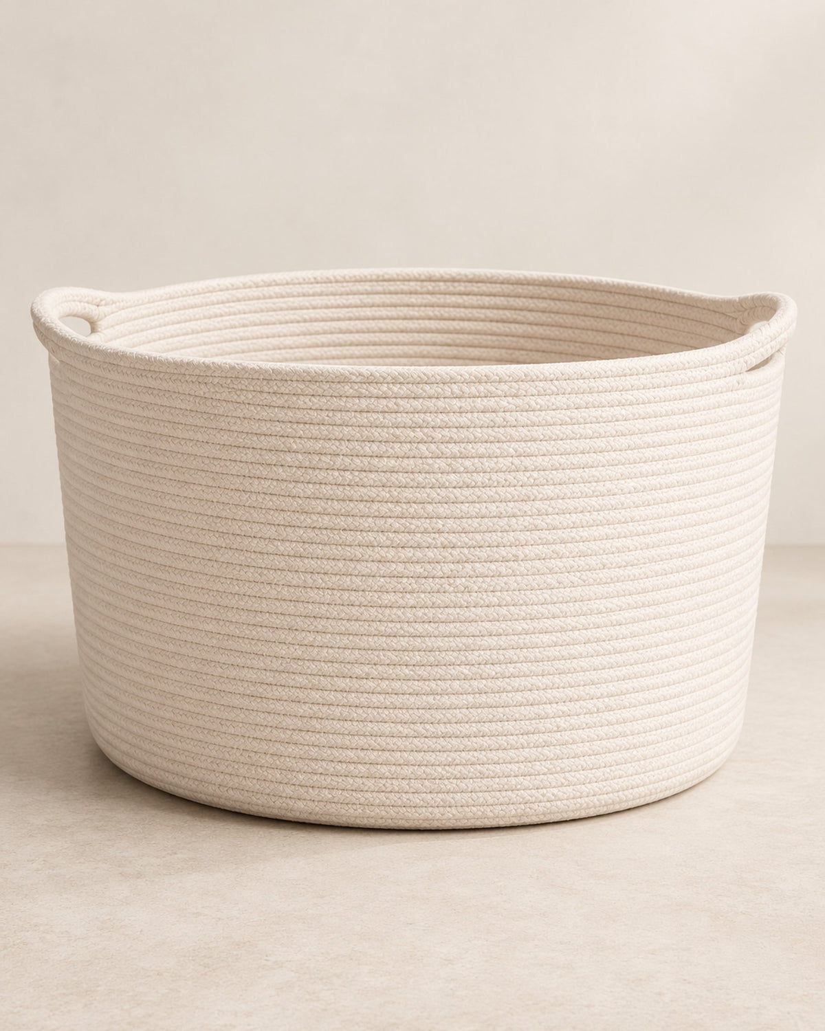 Empty cream cotton rope basket on a warm off-white floor.