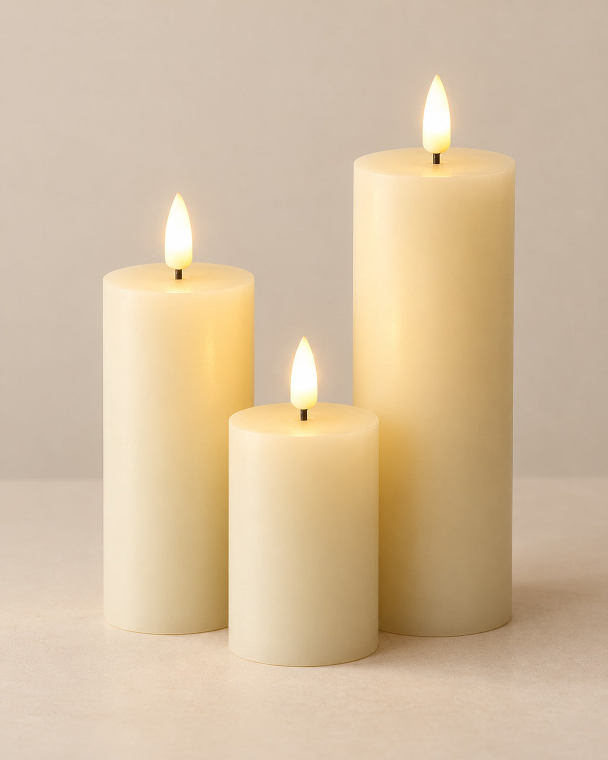 Three ivory LED pillar candles of different heights glowing on a warm off-white surface.