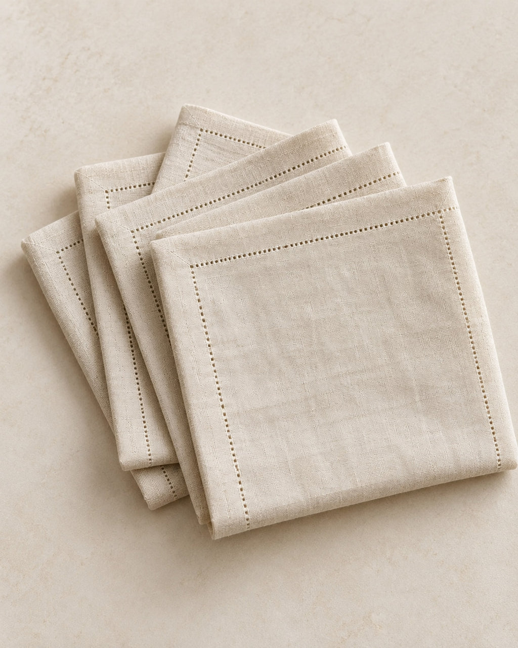 Four natural linen napkins folded in a stack on a warm off-white surface.