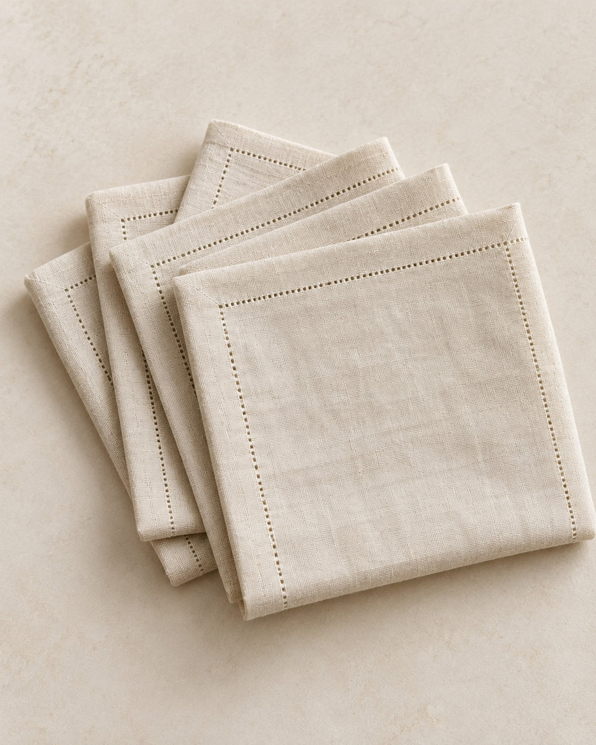 Four natural linen napkins folded in a stack on a warm off-white surface.