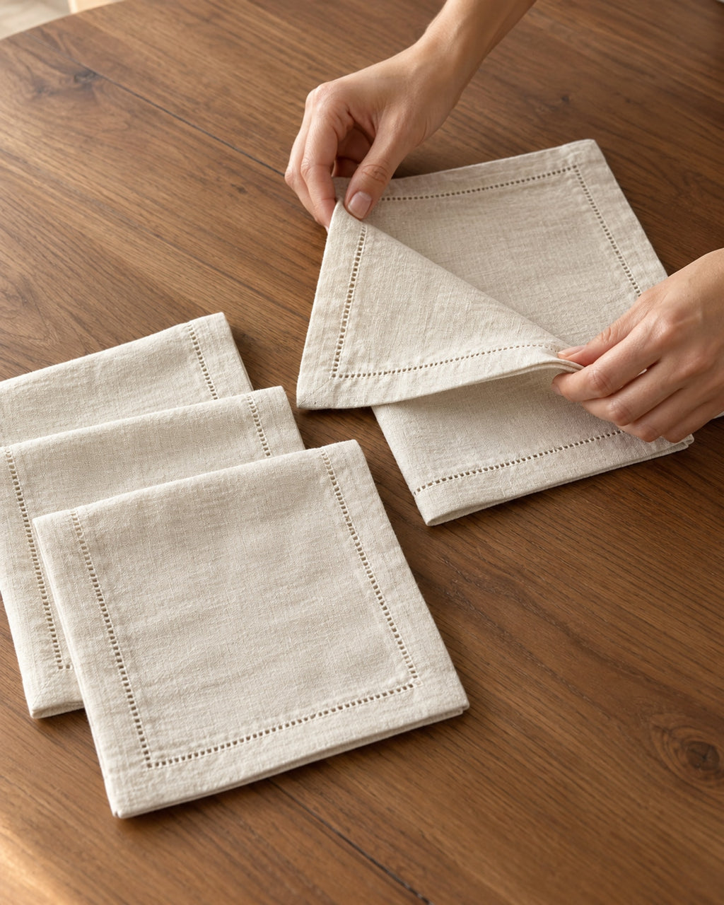 Hands folding a linen napkin on a wooden table.