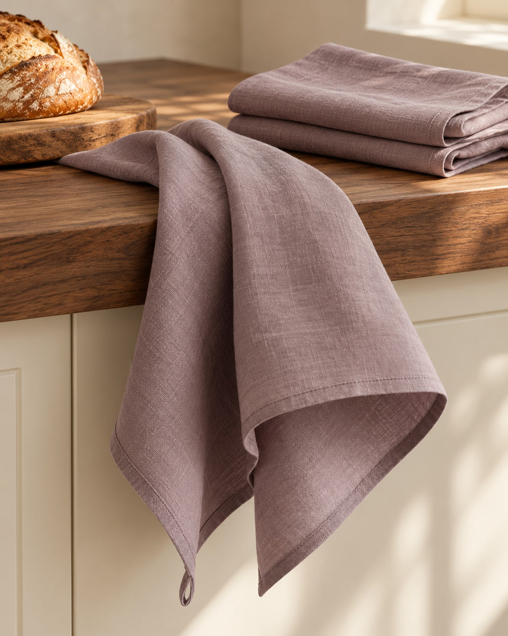 Linen tea towel over the edge of a wooden counter beside a bread board.