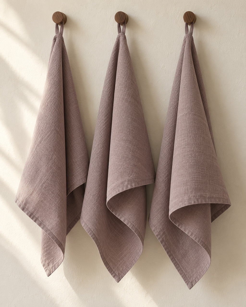 Linen tea towels hanging on wooden hooks in morning light.