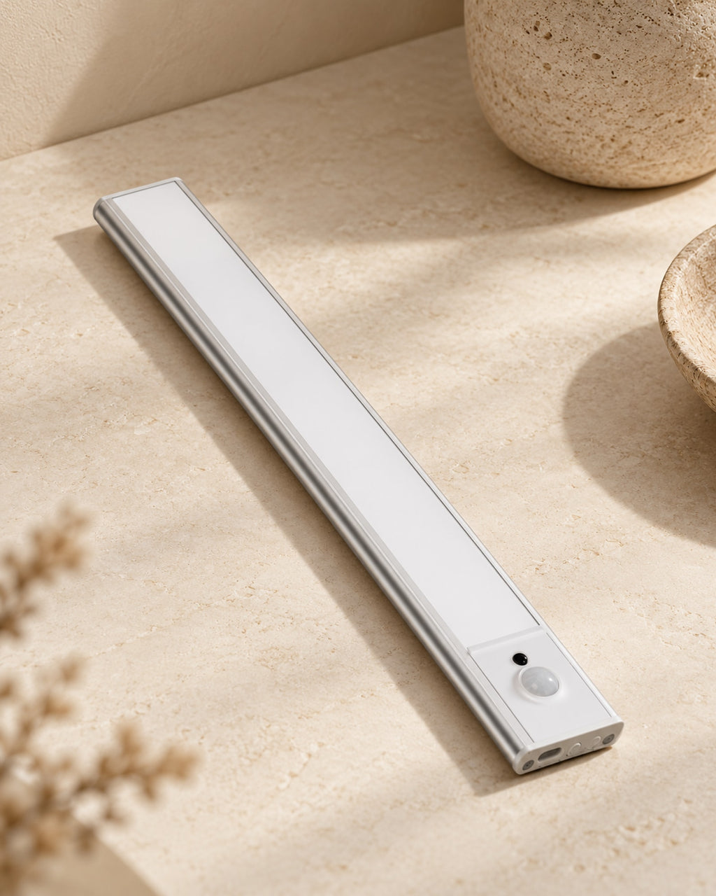 Slim aluminium LED cabinet light with motion sensor, lying on a stone surface