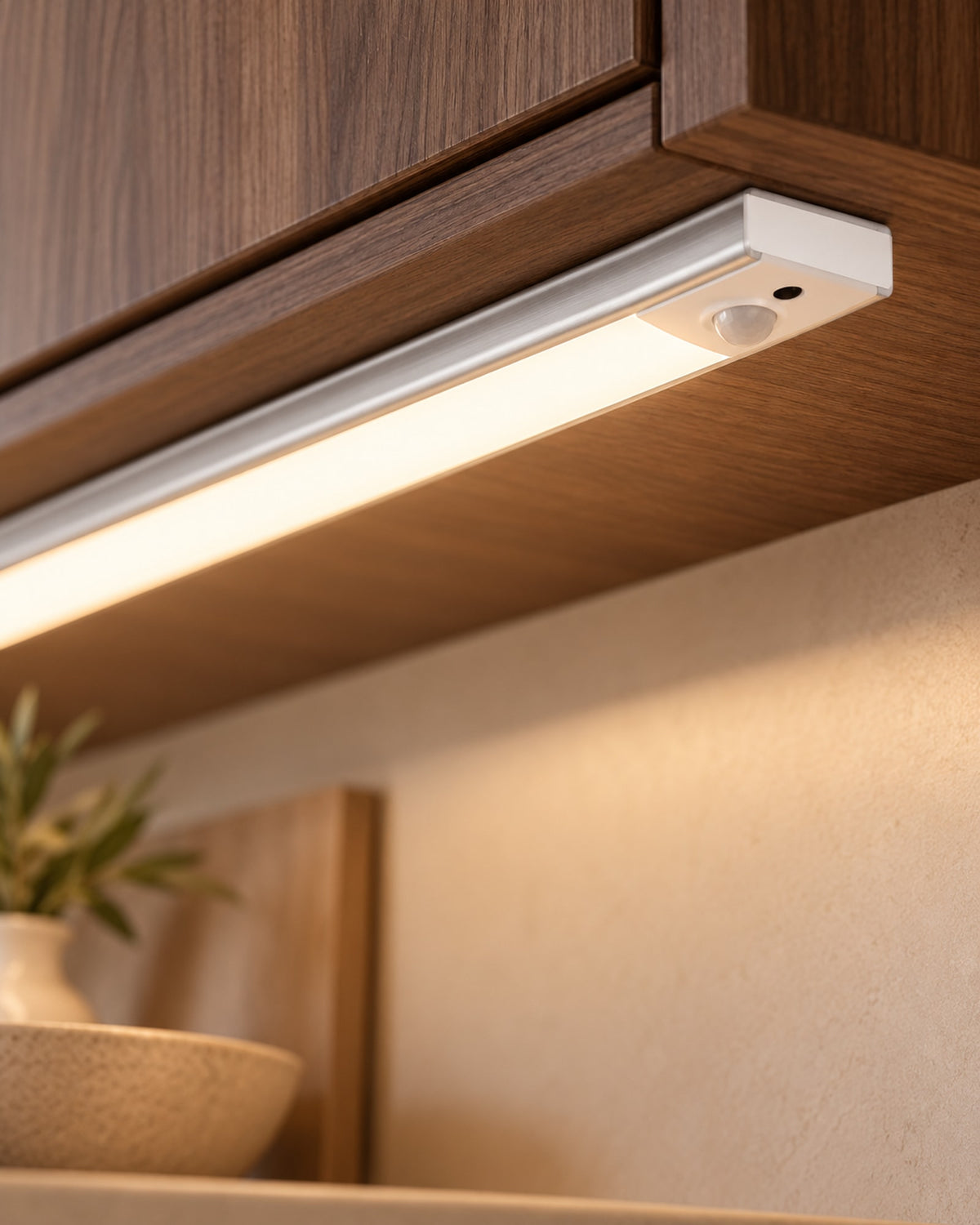 Close-up of the cabinet light switched on under a wooden shelf, motion sensor visible