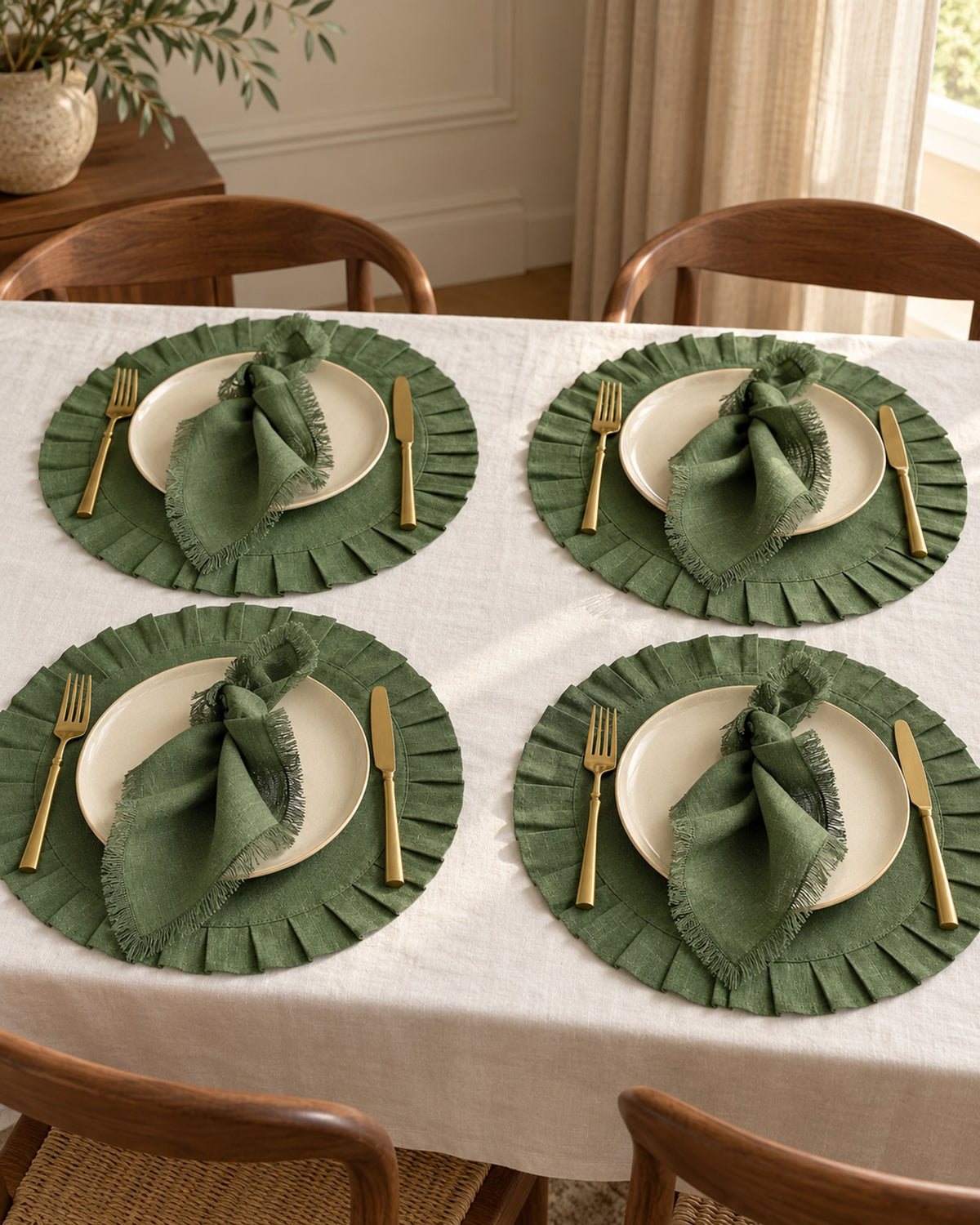 Dining table set for four with green linen placemats and cream plates. Tableware not included.
