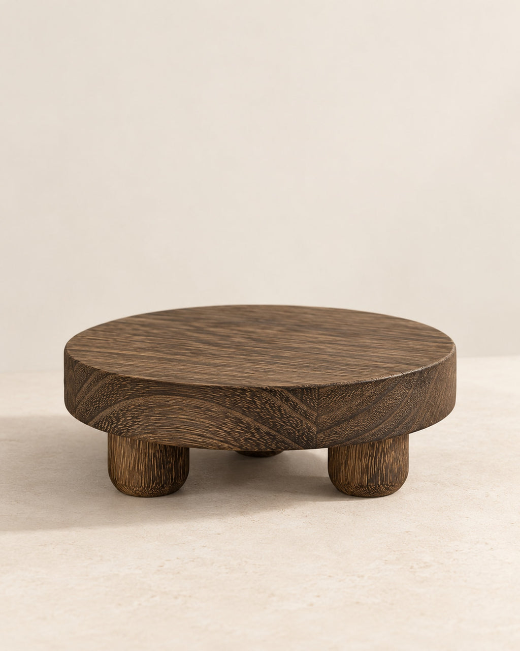 Round dark wooden riser on four feet on a warm off-white surface.
