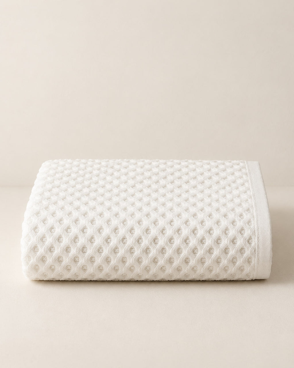 Folded white waffle cotton bath towel on a warm off-white surface.