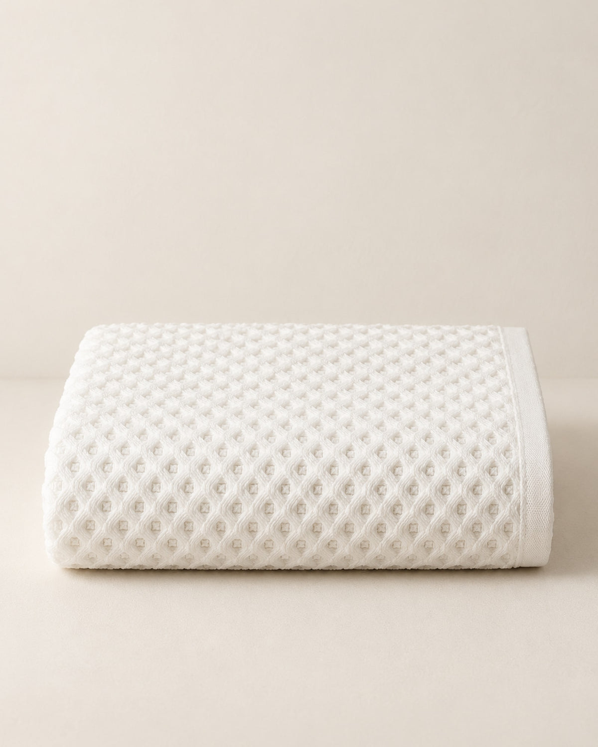 Folded white waffle cotton bath towel on a warm off-white surface.