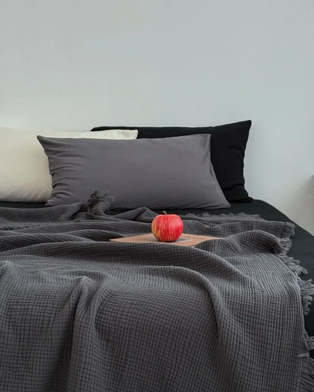 Waffle cotton throw in charcoal grey with fringe, spread over a bed (supplier photo)