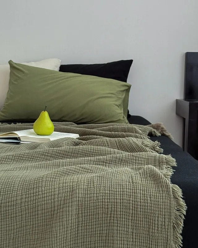 Waffle cotton throw in olive green with fringe, spread over a bed (supplier photo)