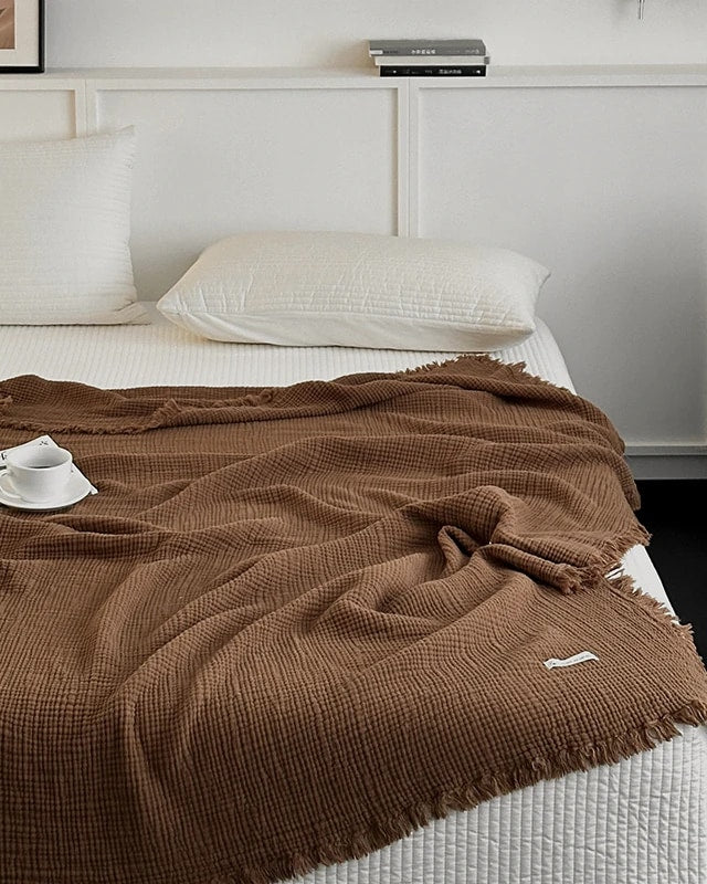 Waffle cotton throw in warm pecan brown with fringe, spread over a bed (supplier photo)