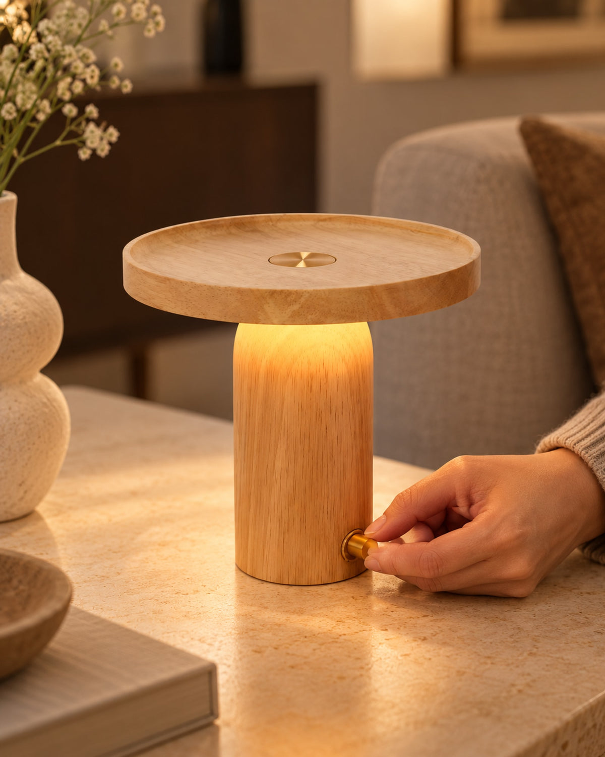 Hand turning the brass rotary switch of the glowing wooden lamp.