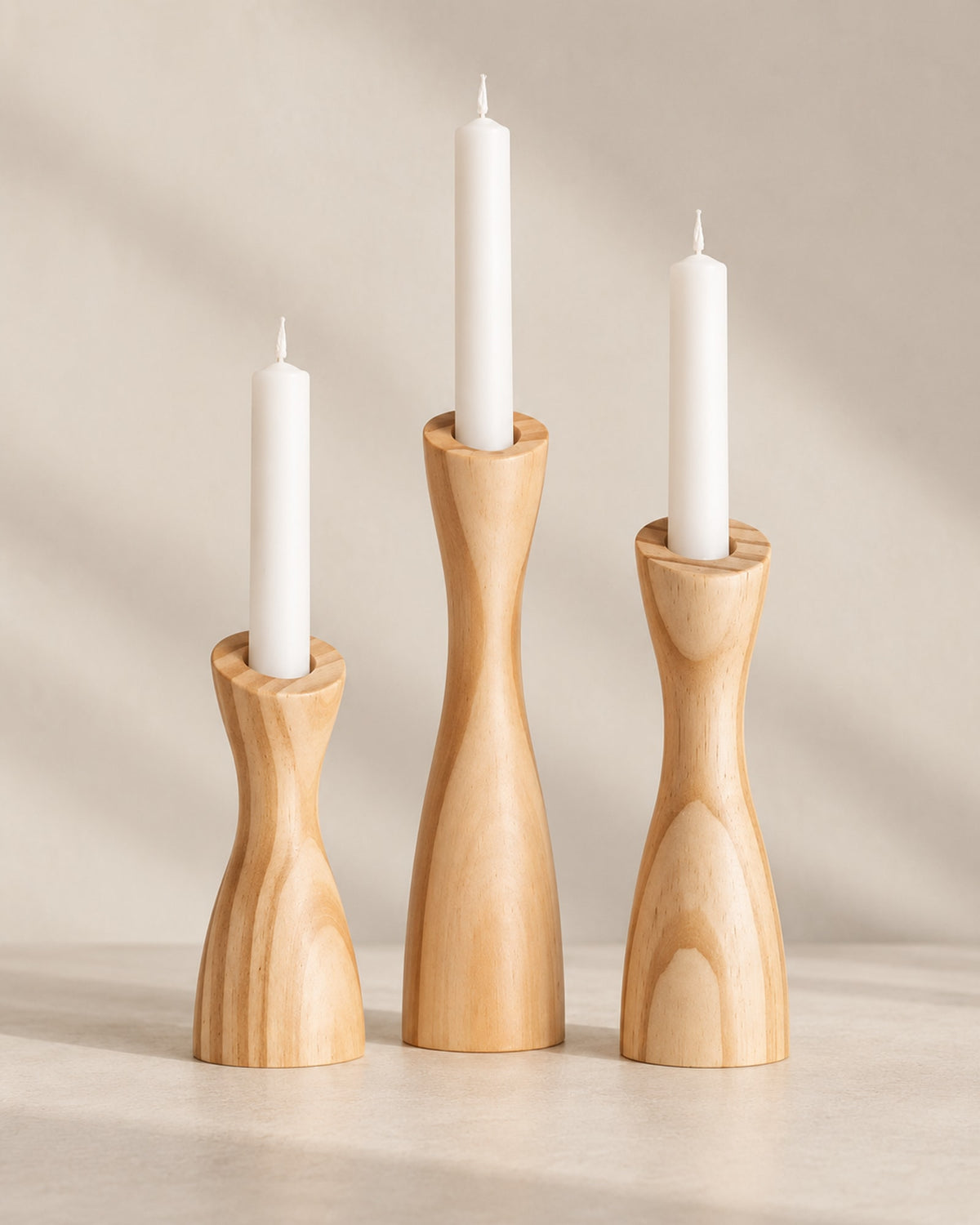 Three light wooden taper candle holders with white candles against a warm off-white wall. Candles not included.