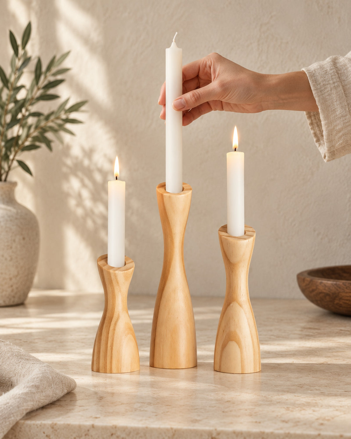 Hand placing a taper candle into the tallest wooden holder.