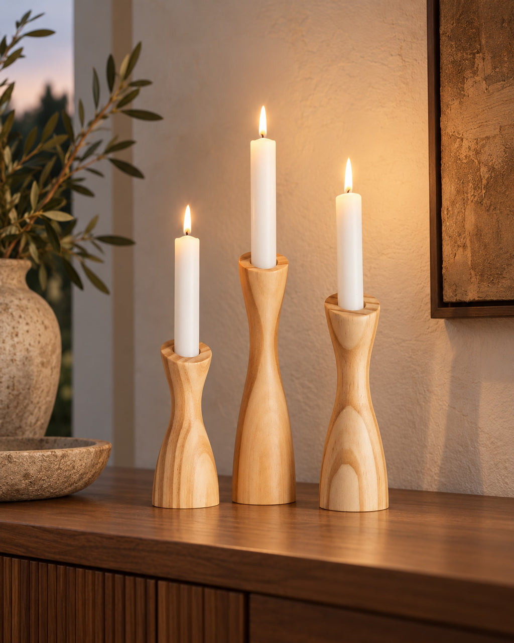 Wooden candle holders with lit candles on a sideboard at dusk. Candles not included.