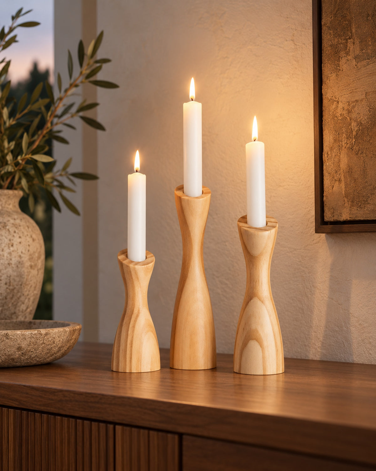 Wooden candle holders with lit candles on a sideboard at dusk. Candles not included.